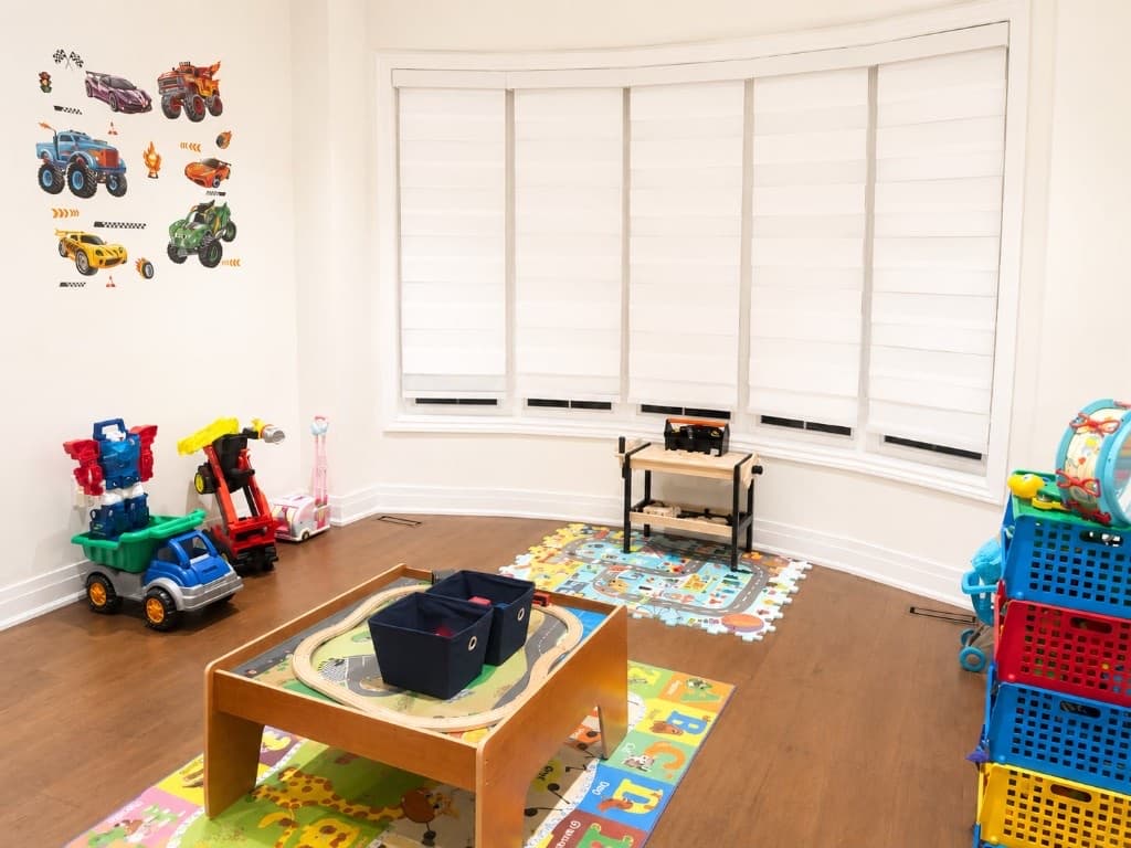 Wooden train table and ride-on toys by a sunny bay window